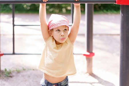 little girl exercising on a horizontal bar in a city park on a summer day.の写真素材