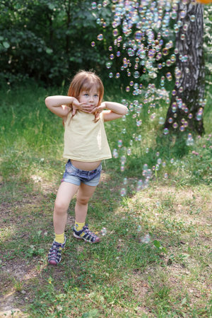 emotional little girl posing in a cloud of soap bubbles on a hot summer day