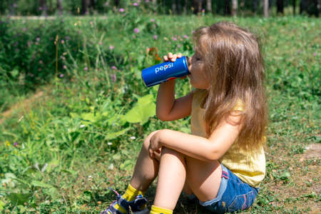 11/07/2021 Moscow, Russia A little girl in a yellow T-shirt drinks Pepsi Cola in the park on a hot summer dayのeditorial素材