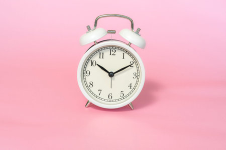 white alarm clock on pink background, minimalistic concept