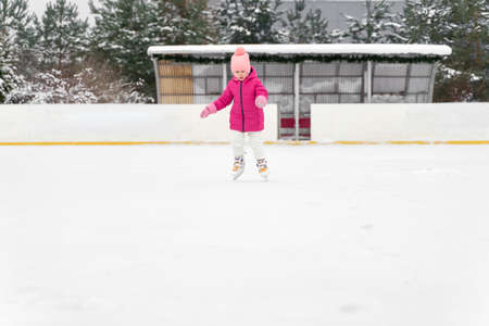 cute little girl in a hat with a bumbon on ice skates on a winter dayの写真素材