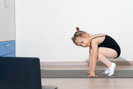 kid girl has a gymnastics lesson with a trainer remotely. Online distance learning. Self-isolation...