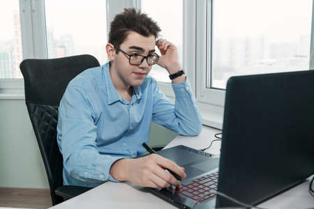 caucasian teenager guy thought about solving a problem while sitting at his workplace with a laptop and a graphic tabletの写真素材