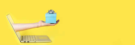 Giving a gift from the screen of the computer online yellow background and blue present with the silver bow on the top of itの写真素材