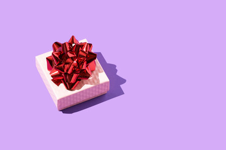 Pink gift box with red bow on the purple background
