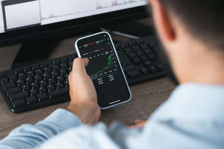 Stock market phone in the hand and desktop computer green and red chartsの写真素材