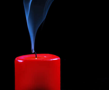 Burning red candle with fading flame and smoke on a black background.の写真素材