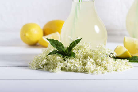 Elder lemonade - healthy and refreshing summer drink. Close up of homemade elderflower syrup in a bottle with elderflowers. Summer drink Hugo Champagne drink with elderflower syrup, mint and lime.の写真素材