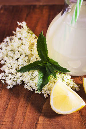 Elder lemonade - healthy and refreshing summer drink. Close up of homemade elderflower syrup in a bottle with elder flowers. Summer drink Hugo Champagne drink with elderflower syrup, mint and lime.の写真素材