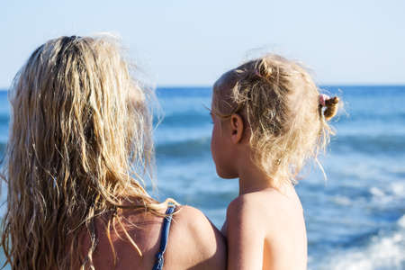 Happy little blond girl in mom's arms on the beach. concept of a happy family. vacation concept. soft focusの写真素材