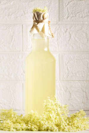 Elder lemonade - healthy and refreshing summer drink. Close up of homemade elder flower syrup in a bottle with elderflowers. Summer drink Hugo Champagne drink with elderflower syrupの写真素材
