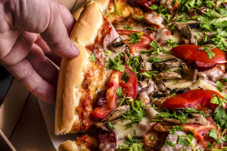 Junk food, calories. Homemade Pizza With Fresh Tomato ham Mushroom Cheese. Pizza time. Man hand taking pizza slices out or box.の写真素材