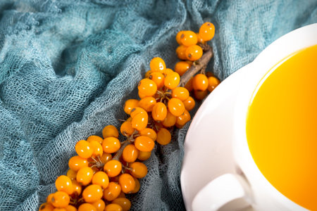 sea-buckthorn tea in white cup with berries with branch on natural green napkin. a source of...