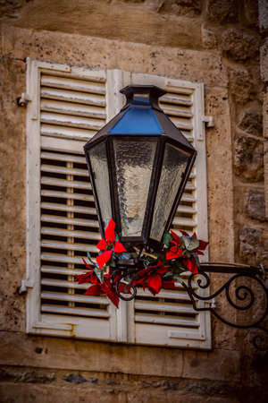 Old lantern, medieval street light with red flowers in the street on the light background in Budva Montenegroの写真素材