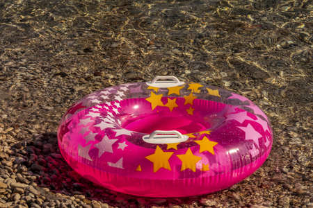 Summer beach composition. Pink inflatable float with stars on pebble, shingle, boulder sea background, trendy summer sea concept. Soft focus.の写真素材