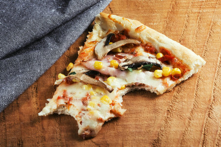 a piece of pizza bitten off on wooden surface near the napkin. Fast food, junk food concept. Meat,...