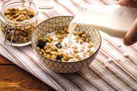 Breakfast food background. Milk Pouring Over Granola on light table napkin, Healthy vegetarian...