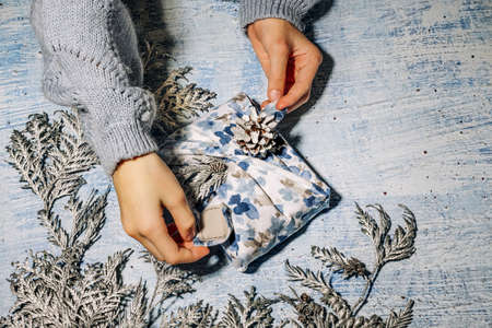 Girl prepare Xmas Blue hand made gift package for Christmas with fabric thuja and cone. Zero waste gift wrapping traditional Japanese furoshiki style. Ecological concept eco-friendly decor xmas.の写真素材