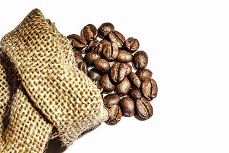 Roasted coffee beans scattered from burlap bag isolated on white background. Copy space.の写真素材