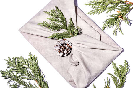 Zero waste gift wrapping traditional Japanese furoshiki style. Beige hand made gift package for Christmas with fabric, thuja and cone on white. Ecological concept eco-friendly decor xmas. Close upの写真素材