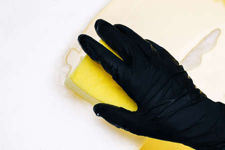 Close up on womans hand in protective black rubber gloves cleaning with yellow sponge...の写真素材