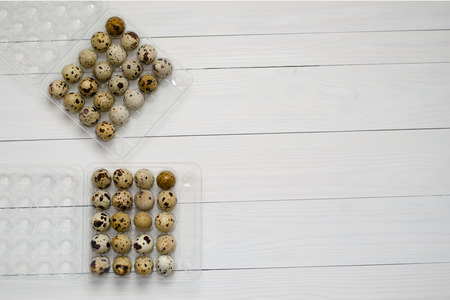 Quail eggs in a plastic container on a white wooden background. The view from the top. Copy spaceの写真素材