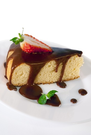 A piece of sponge cake with chocolate sauce,strawberry and mint on a white plate on white isolated backgroundの写真素材