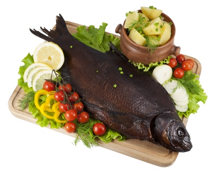 Smoked bream on a wooden board with a hot potato in a clay pot, tomatoes, lettuce, slices of lemon and yellow paprika, onion and dill の写真素材