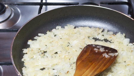 Sliced onion fried in a pan and wooden spoonの写真素材