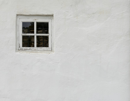 The old white plastered wall with a small window as backgroundの写真素材
