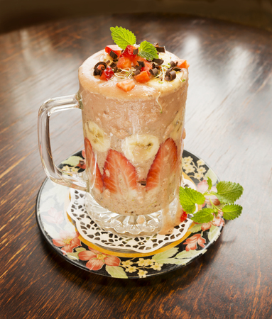 Healthy fresh strawberry and banana smoothie with lucerne sprouts, strawberry pieces, chocolate and mint on old vintage table.の写真素材