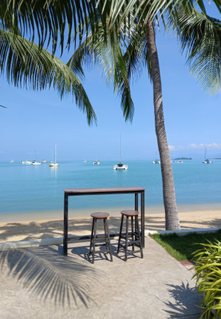 Table and chairs on the beach in Koh Samui, Thailand. Ocean landscape with boats as background.の写真素材