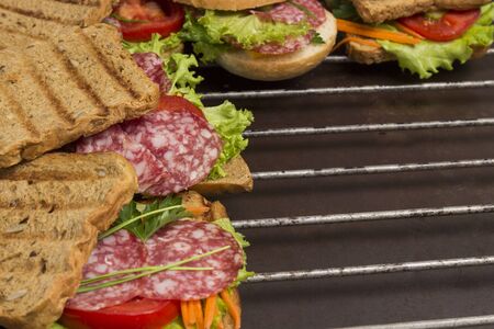 Grilled sandwich with salami, cheese tomatoes and greens on metal grill.の写真素材