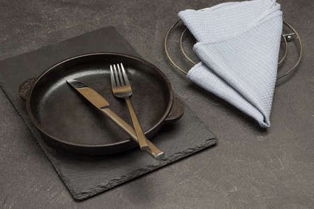 Gray napkin on table. Spoon and fork in empty cast iron skillet. Black background. Top viewの写真素材