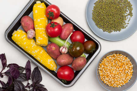 Vegetables on pallet, swing of yellow corn, tomatoes, potatoes. Corn grains and mung bean in plates. Sprigs of parsley on table. White background. Flat layの写真素材