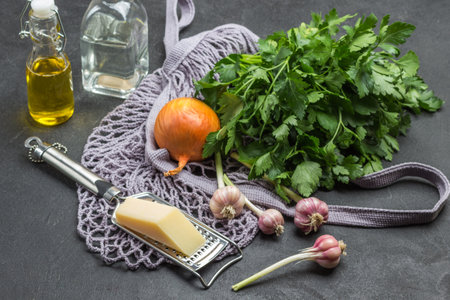 Mesh fabric bag with groceries. Two bottles of oil and water. Garlic, onion and cheese on grater, sprig of parsley. Black background. Top viewの写真素材