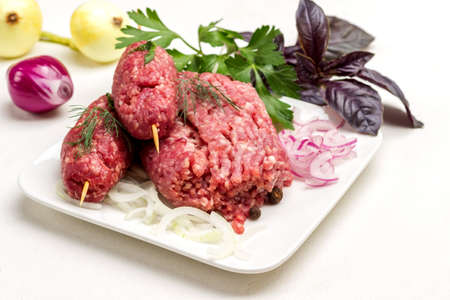 Raw minced meat on wooden skewers and onion sliced into rings. Kebab cooking. Basil leaves and onion head. White background.の写真素材
