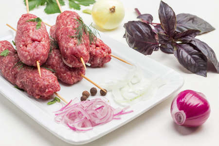 Raw minced meat on wooden skewers and onion sliced into rings. Kebab cooking. Basil leaves and onion head. White background.の写真素材