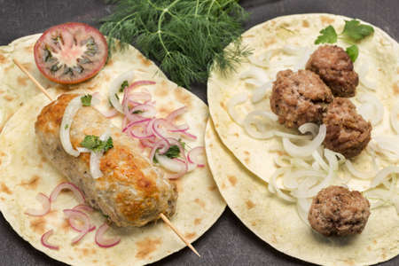 Kebab on skewer and meatballs with tomatoes and onions on pita. Dill sprigs. Close up. Black background. Flat layの写真素材