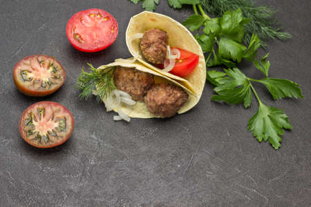 Pita with meatballs and onions. Chopped tomatoes on table. Copy space. Black background. Top viewの写真素材