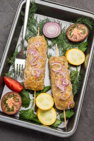 Ready-to-eat meat kebab with vegetables and herbs in tray. Black background. Flat layの写真素材
