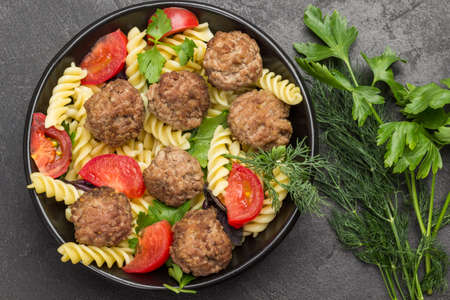 Meatballs with tomatoes and pasta in black bowl. Dill and parsley sprigs. Black background. Flat layの写真素材