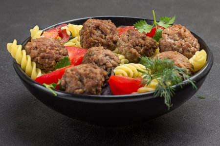 Meatballs with tomatoes and pasta in black bowl. Black background. Top viewの写真素材