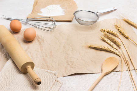 Brown paper on table. Sieve, whisk and rolling pin. Flour on paper, Eggs and spikelets of wheat. White background. Top viewの写真素材