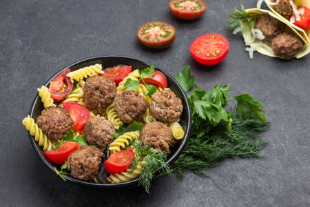 Meatballs with tomatoes and pasta in black bowl. Dill and parsley sprigs. Pita with meatballs and onions. Black background. Flat layの写真素材