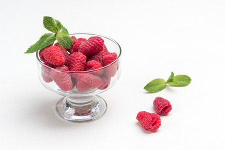 Ripe raspberries in glass bowl. Mint leaves and berry on table. Copy space. White background. Top view.の写真素材