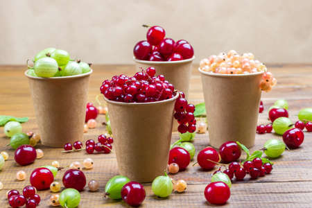 Currants, gooseberries and cherries in paper cups. Berries on table. Wood backgroundの写真素材