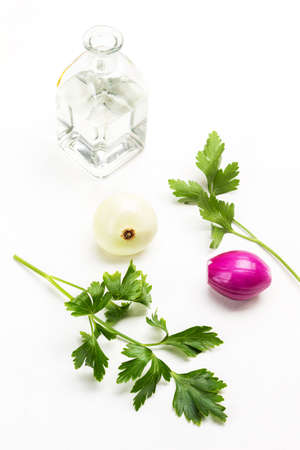 Parsley leaves, two heads of white and blue onions. Glass bottle with water. White background.の写真素材