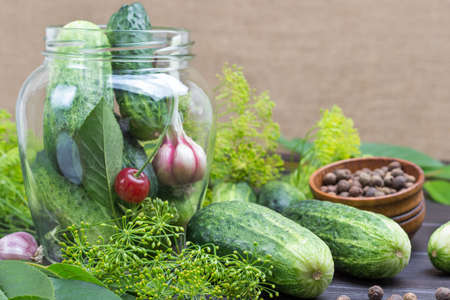 Garlic, cucumbers and cherries in glass jar. Cucumbers and dill on table. Homemade Fermentation Productsの写真素材