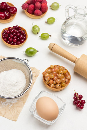 Flour in sieve, egg in bowl. Tartlets with berries. White background. Top viewの写真素材